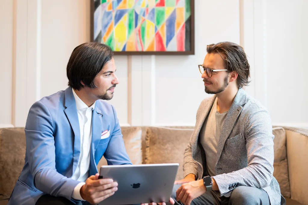 Dr. Khorsand berät einen Kunden auf dem Sofa, Internationale Promotionsberatung, Coaching-Gespräch mit iPad