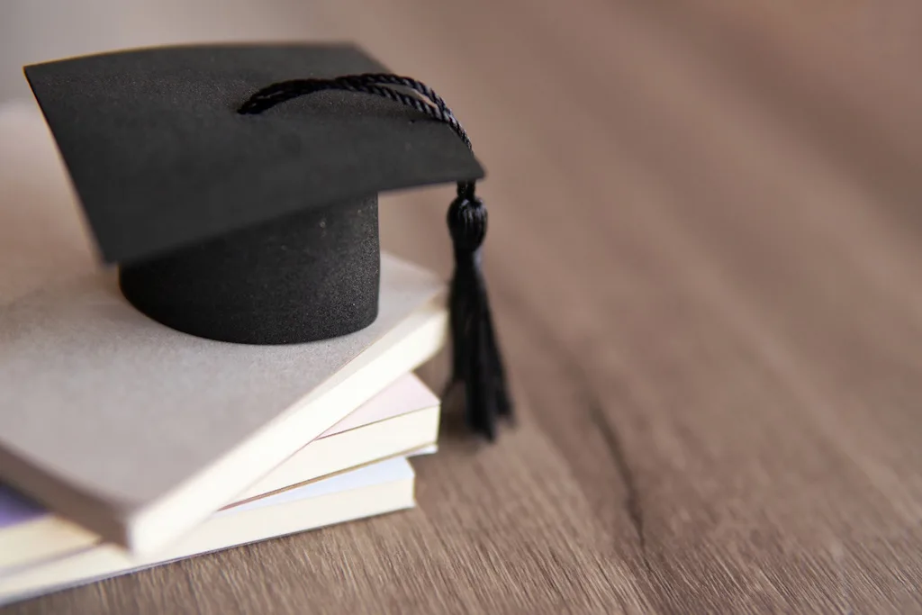 Schwarzer Doktorhut mit Quaste auf weißem Bücherstapel, Symbol für akademische Beratung und Promotion