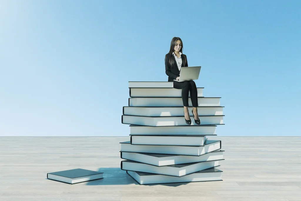 Beraterin sitzt auf einem Bücherstapel mit Laptop – Internationale Promotionsberatung Coaching